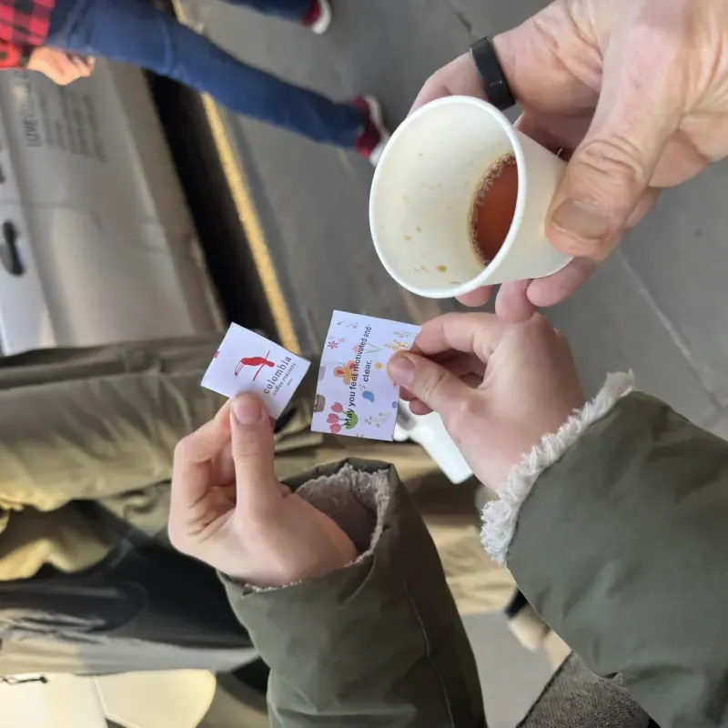 Hands holding a coffee cup with a small printed fortune card reading 'May you feel motivated and clear', May Morning 2026