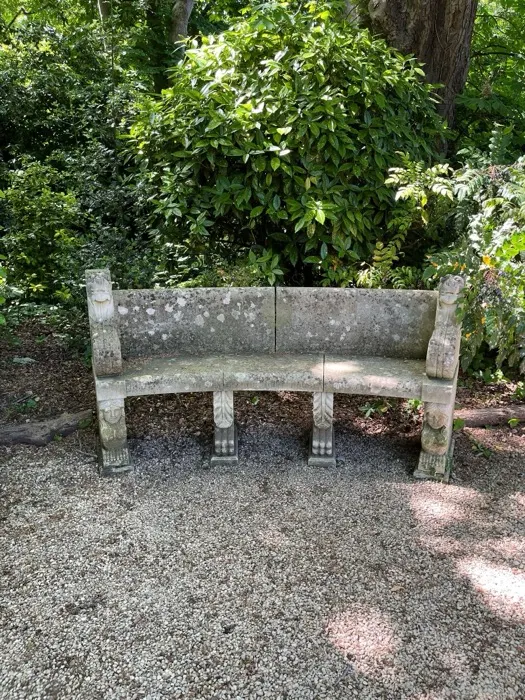 Weathered stone bench with carved supports in a leafy corner of Worcester College gardens